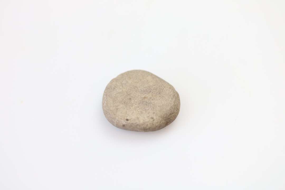 Spillebrik af flad sten. Diameter: 2,6 cm.